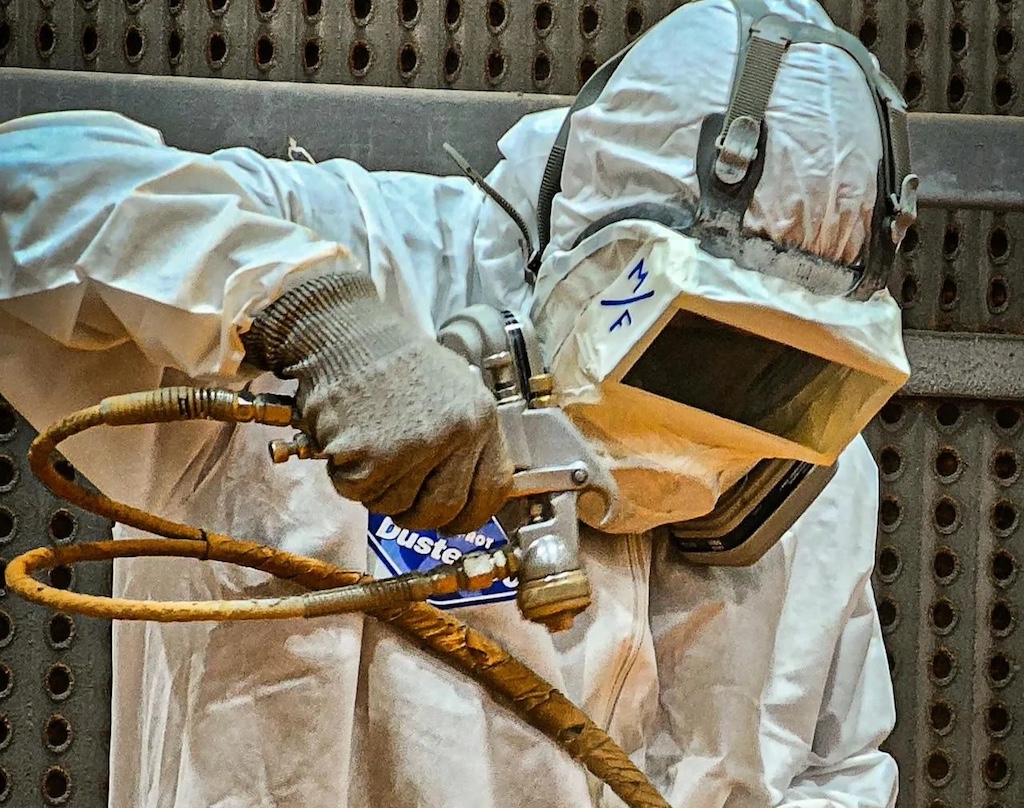 Industrial worker sandblasting in protective gear