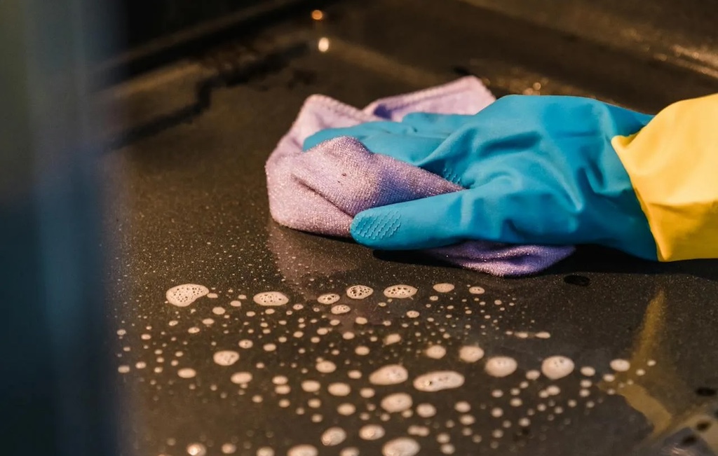 Hand in rubber glove cleaning oven surface