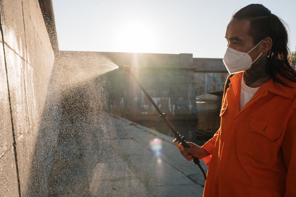 Man in orange robe cleaning gray concrete wall