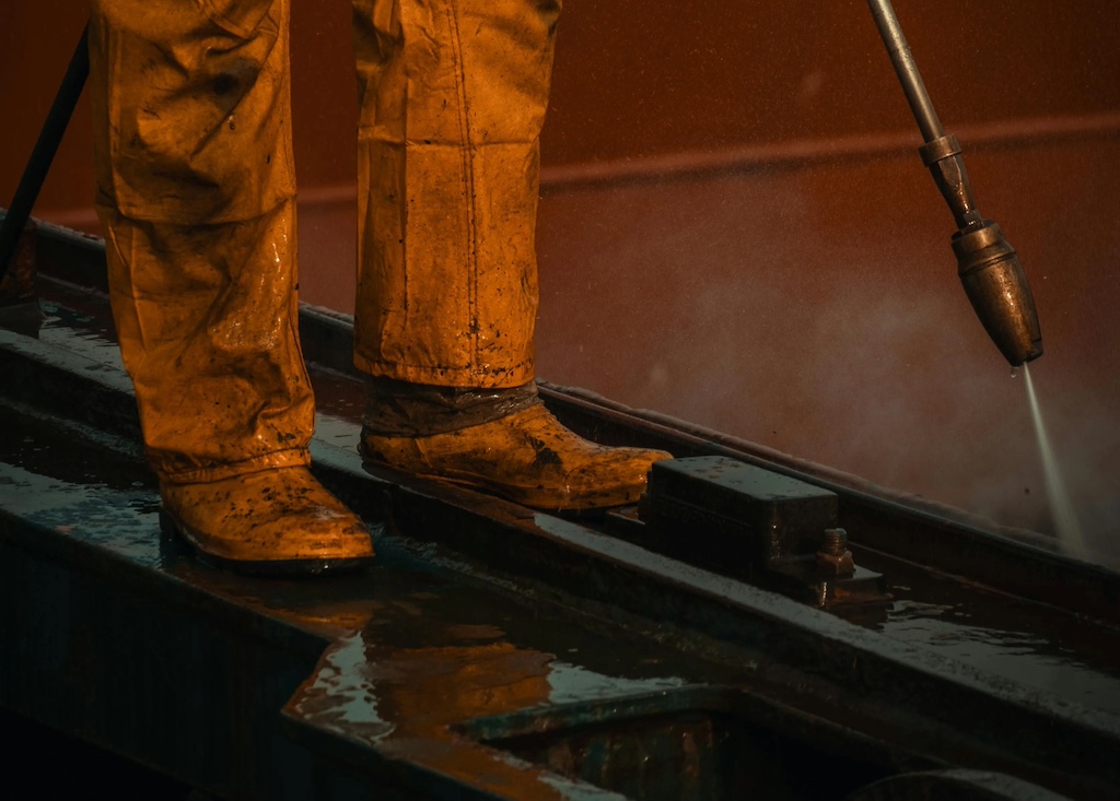 Worker in yellow protective gear using pressure washer
