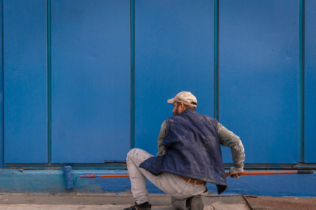 Worker painting a vibrant blue wall outdoors