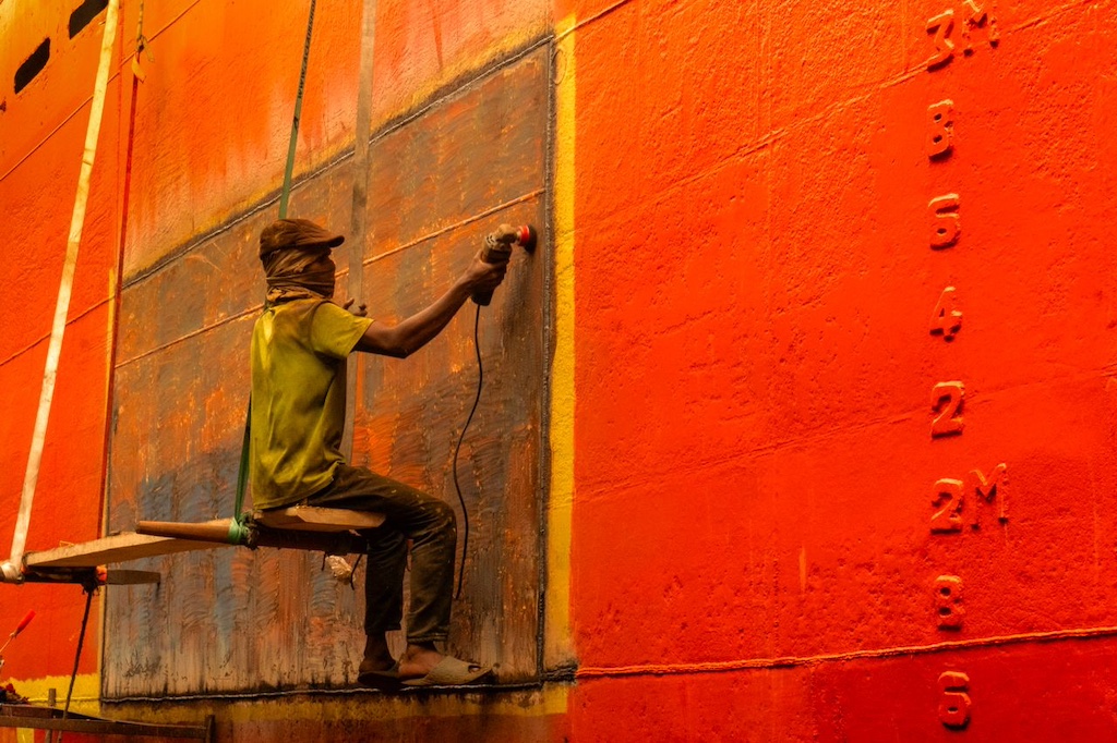 Worker sanding brightly painted ship hull