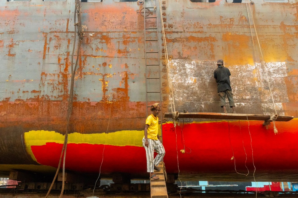 Workers painting rusty ship hull with vibrant colors